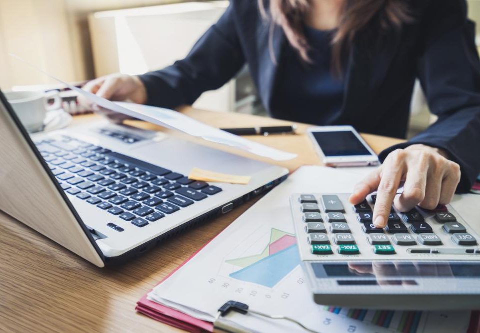 Une personne regardant une feuille devant son pc portable en calculant sur une calculette